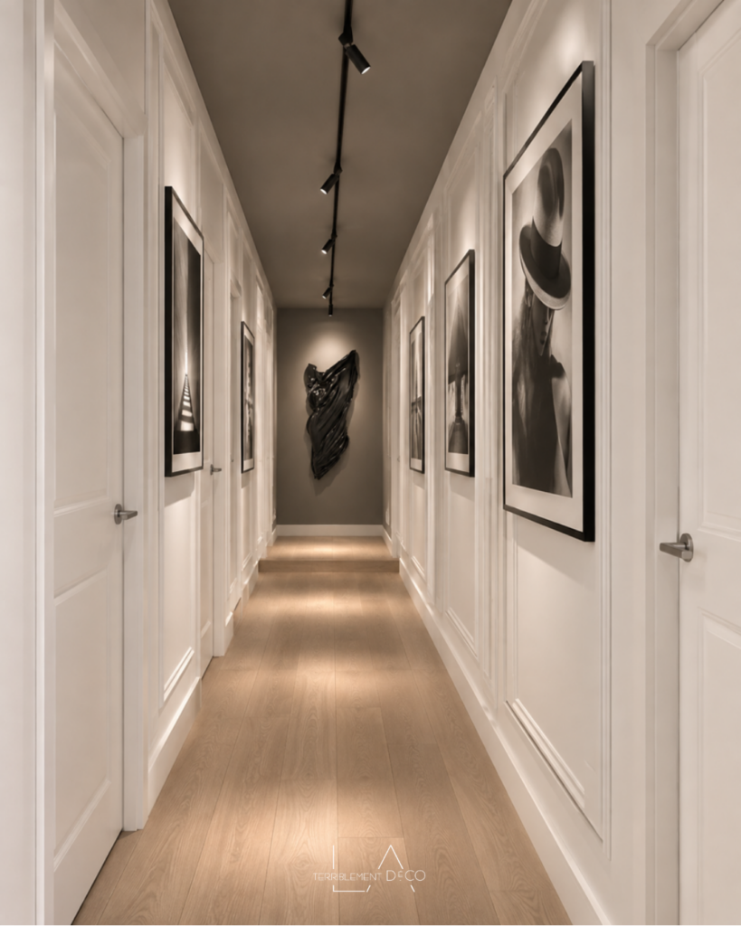Long couloir transformé en galerie d’art avec moulures, œuvres, plafond et mur du fond gris foncé pour rythmer le parcours et atténuer l’effet tunnel