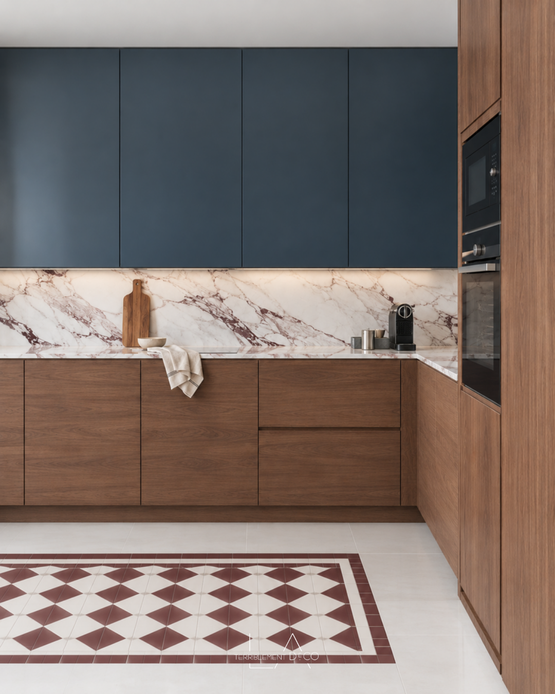 La cuisine contemporaine avec meubles hauts bleu nuit, façades basses en noyer, crédence en marbre blanc veiné brun et tapis de carreaux géométriques au sol, un design de Laurence ARNAUD