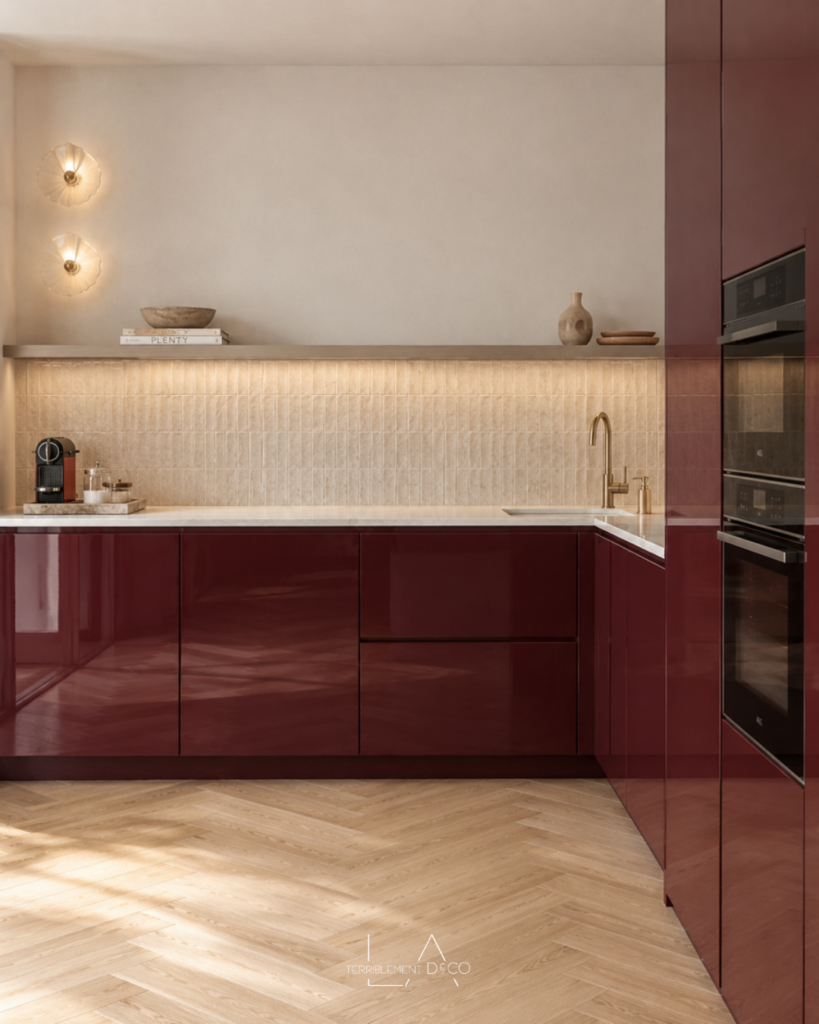 Cuisine en L avec façades rouge bordeaux brillantes, crédence beige texturée, étagère éclairée et parquet clair en point de Hongrie, un design de Laurence ARNAUD